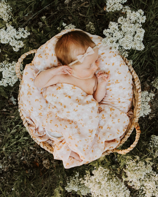 a newborn baby girl laying in a basket, surrounded by wildflowers and wrapped in a pink floral swaddle