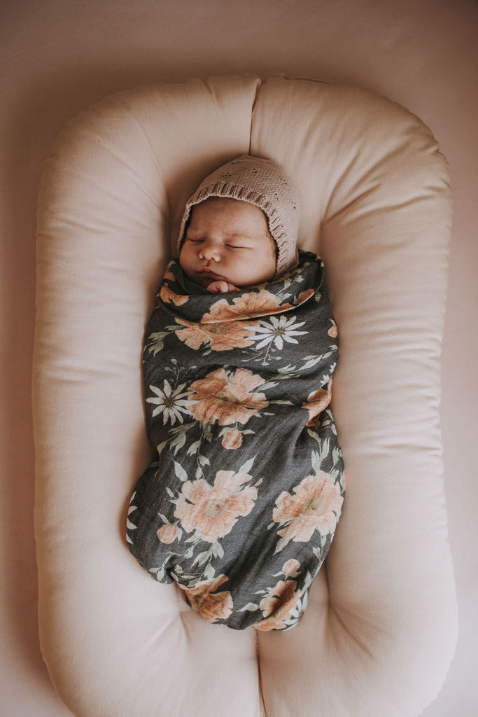 newborn baby girl swaddled in a dark floral peony patterned swaddle, taking a baby nap on a bed covered with pink bed sheets