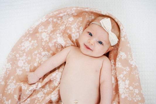 smiling baby girl with a lace bow on a pink floral blanket for valentines day photoshoot