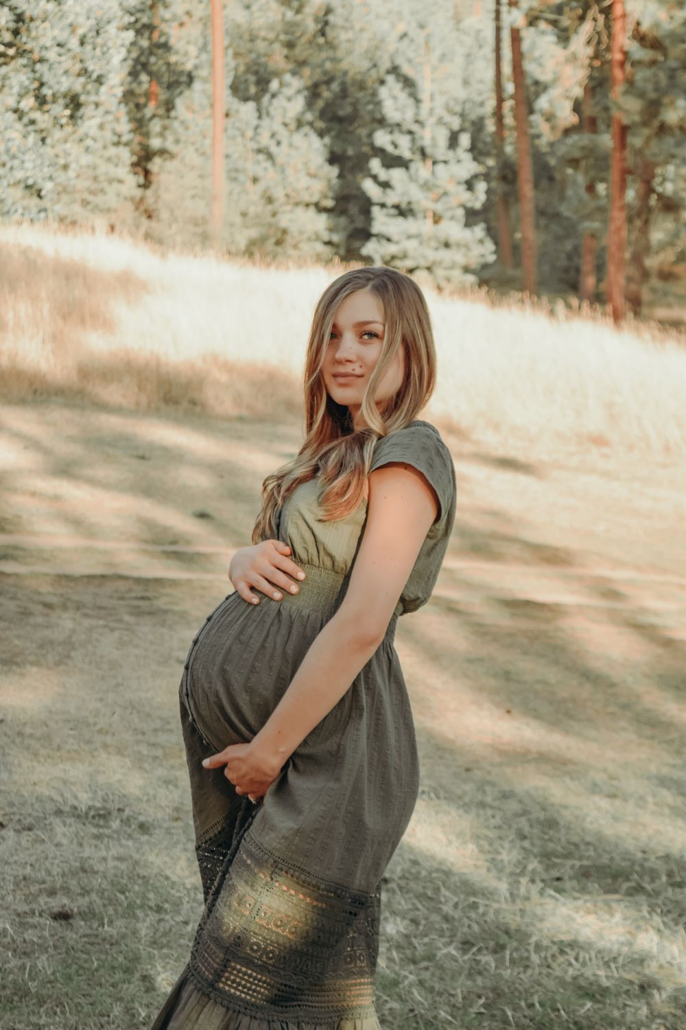 an expecting mom in a green dress holding her baby bump