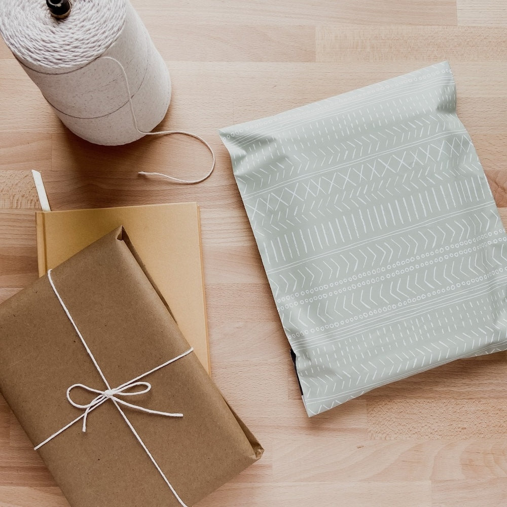 flatlay photo of the pastel green 12x15.5 polymailer shipping bag beside a brown packaging and light brown notebook and roll of twine
