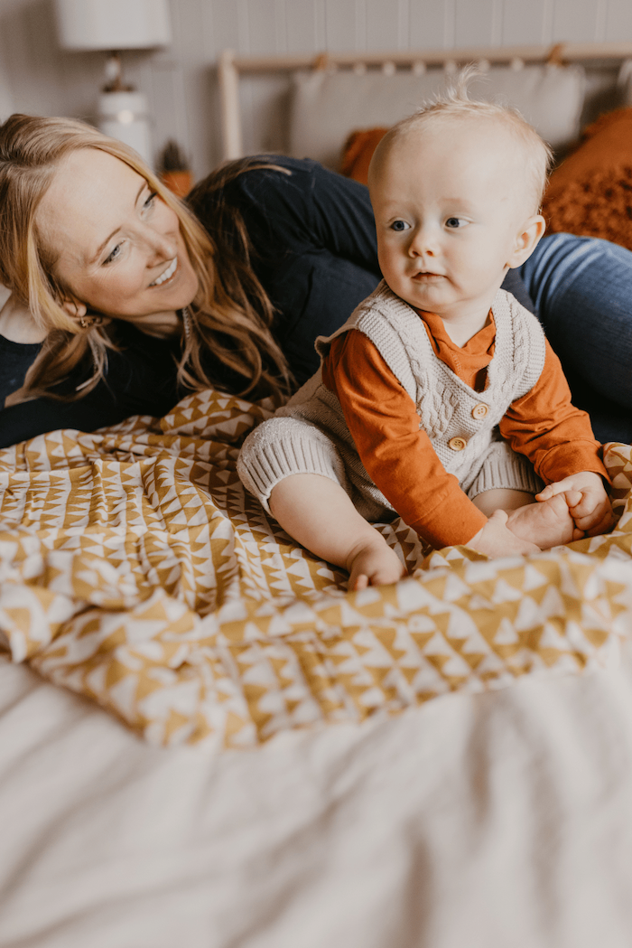 mommy and baby bonding together in the bed, using our mountain swaddle as cover and baby wearing boho baby clothes looking away from the camera