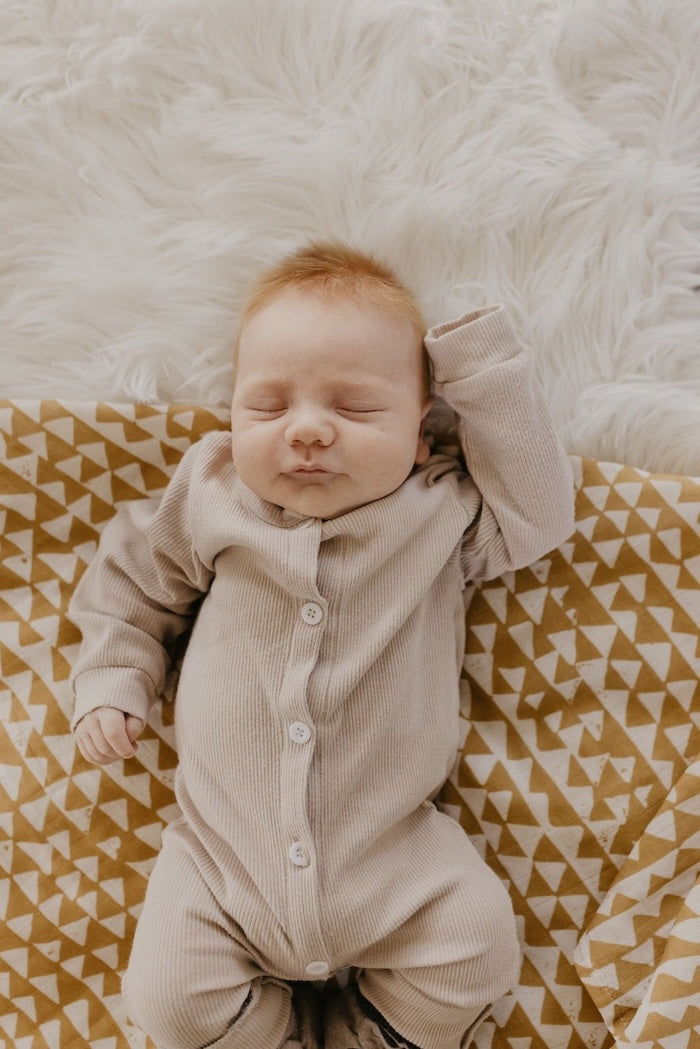 baby sleeping cozily on top of our checkered mountain swaddle in color mustard wearing a taupe boho baby clothes