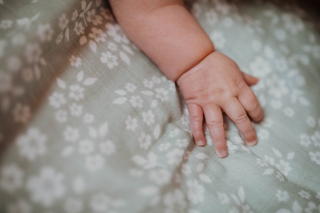 A close-up of a baby's arm resting on a green swaddle with a whimsical floral pattern.