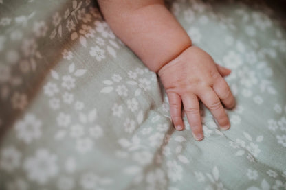A close-up of a baby's arm resting on a green swaddle with a whimsical floral pattern.