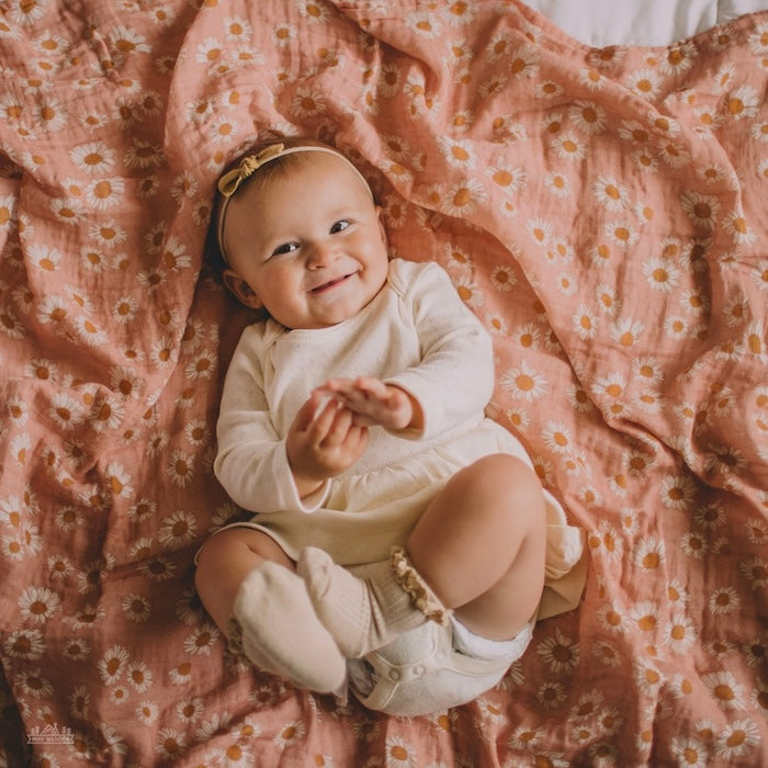 A baby with a brown bow lies on a pink and daisy-patterned swaddle.