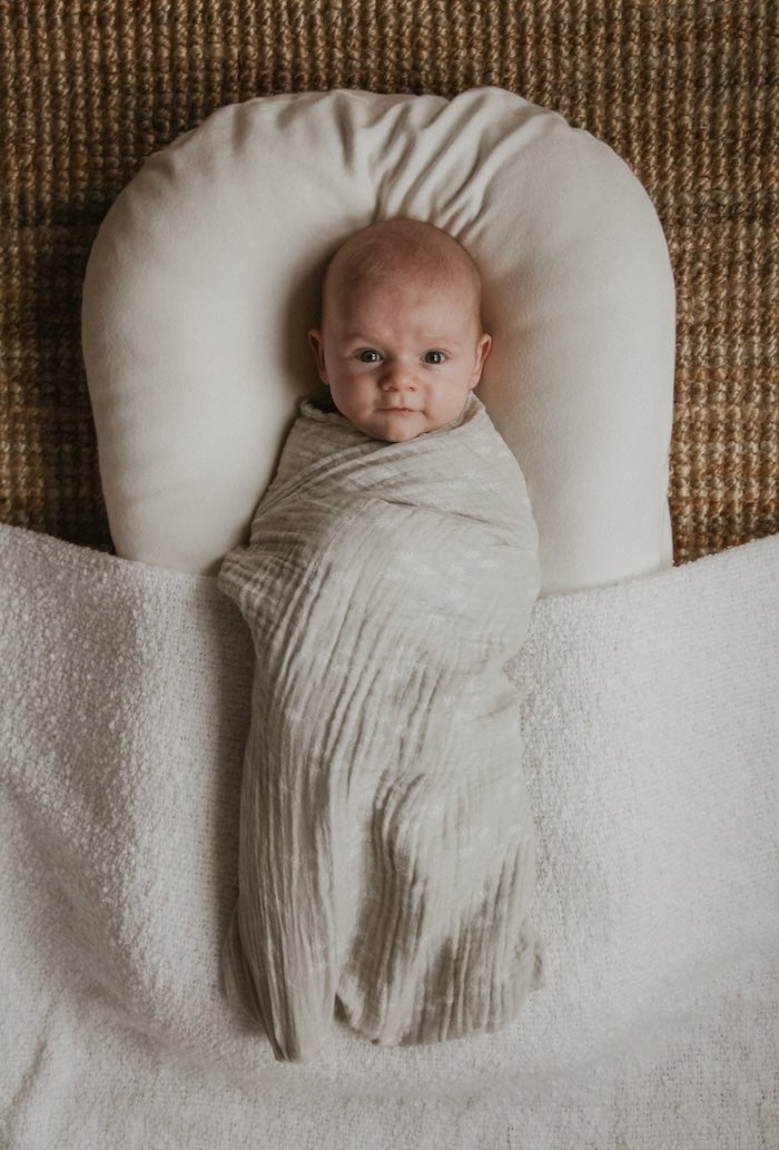 cute baby boy swaddled in a gray neutral swaddle blanket with small pine trees, snuggled cozy in a lounger