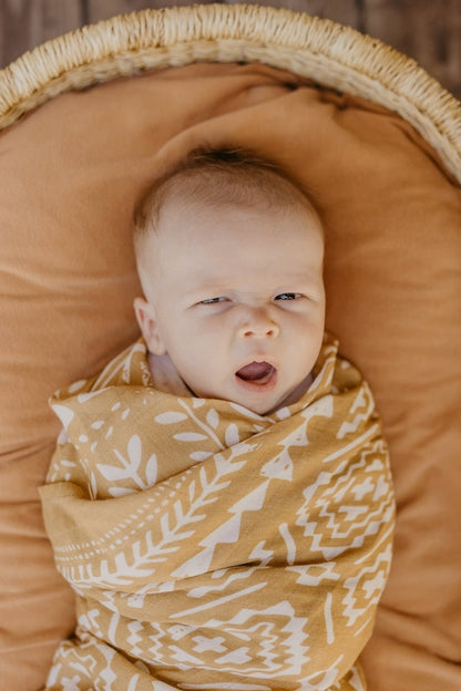 sleepy baby boy wrapped in an orange boho geo swaddling blanket