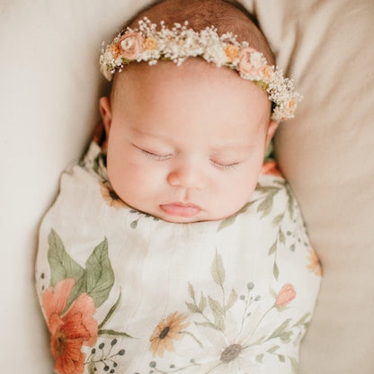 a sweet girl wearing a dainty flower crown headband sleeping soundly and wrapped in her spring blossom white peony swaddle