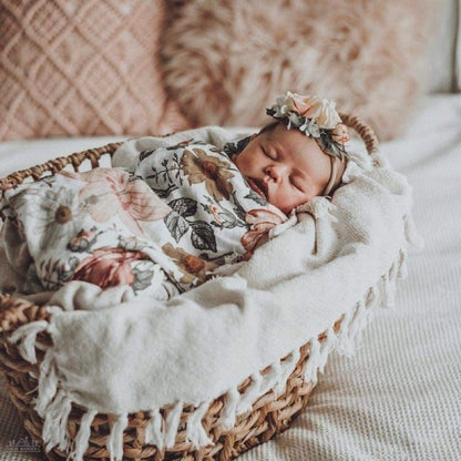 The newly born baby is sleeping peacefully in a baby basket wrapped in a floral swaddle wearing a cute flower crown.
