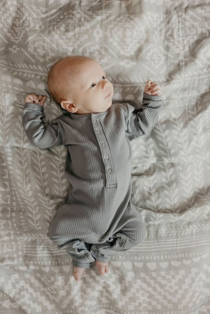 Photo of a little baby boy wearing a green baby onesie lying on his back on top of our neutral receiving blankets the tapestry green spruce boy swaddle