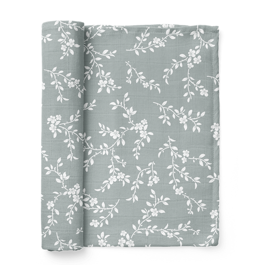folded bloom floral muslin swaddle showing the little white leaves and flowers in a nice blue background