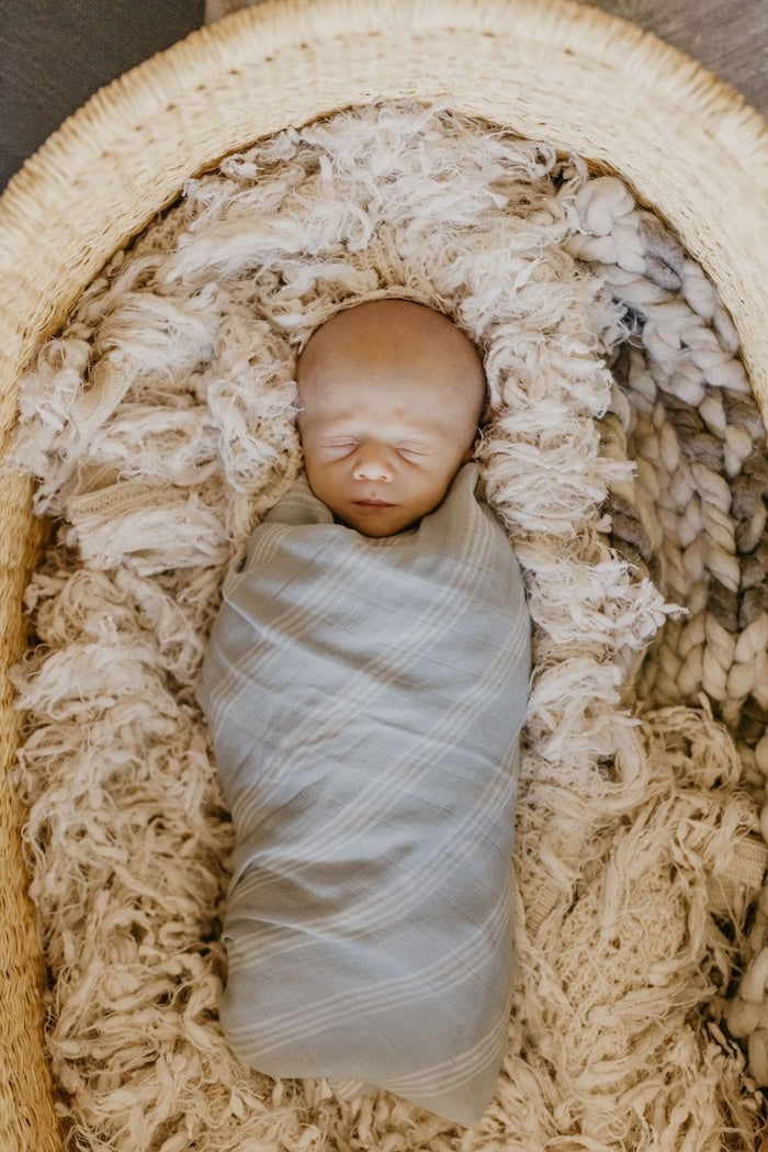 sweet little boy sleeping in a bassinet wrapped with our stripe baby swaddle made with high quality cotton muslin fabric