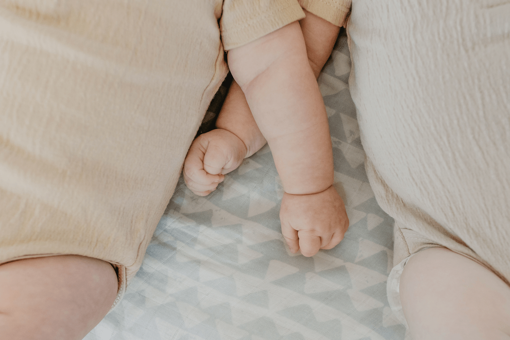 babies wearing neutral colored baby clothes lying on top of the blue swaddle blanket arms are crossed