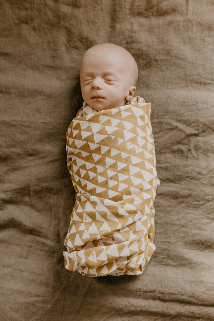 sleeping newborn baby wrapped securely in our mountain swaddle which looks perfect for the adventure themed nursery. Trending checkered print.