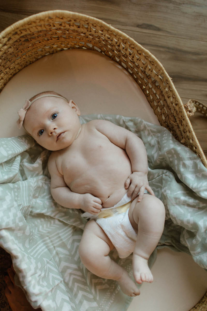 baby girl with a light green blanket in a boho moses basket