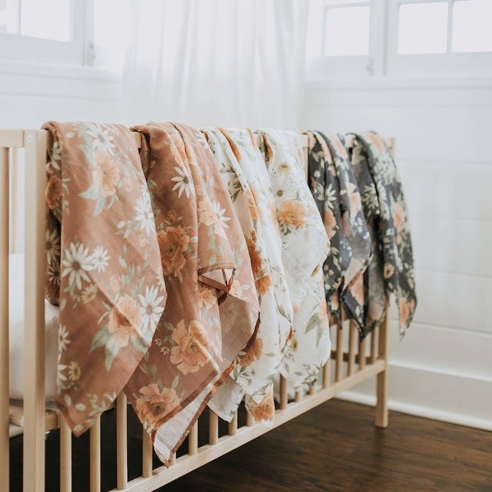 a boho nursery with a nice wooden crib and with the spring blossom clay muslin baby swaddles in three colors hanging on top of the crib with half of them dangling showing the beauty of the blankets