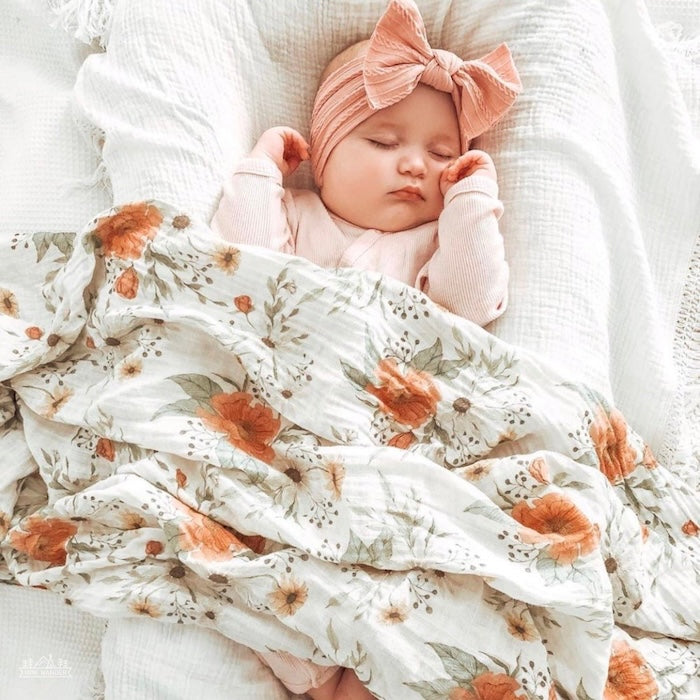 a beautiful photo of a cozy baby sleeping in her baby lounger wearng a peach ribbon headband with her body using the peony swaddle as a blanket