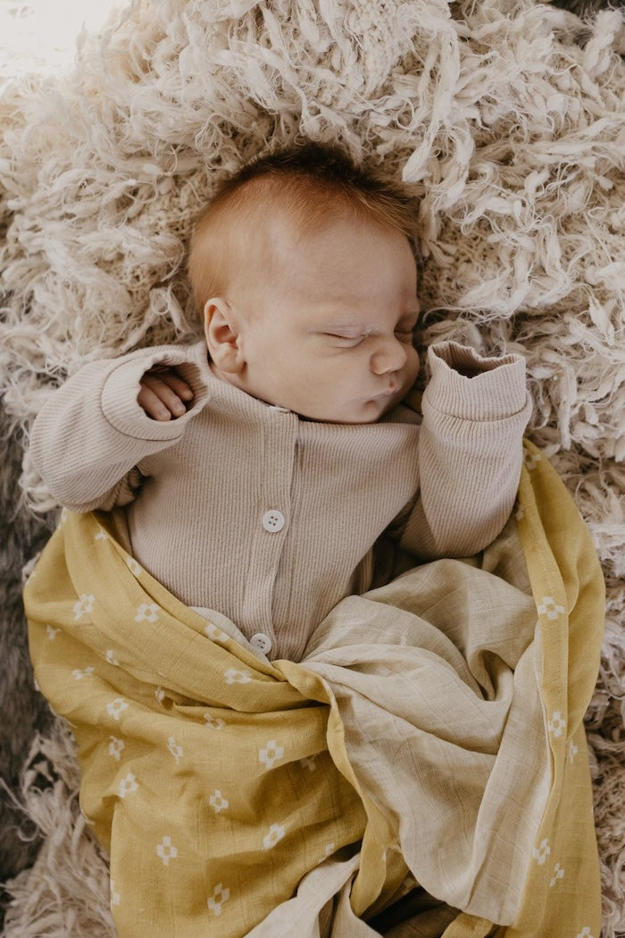 sleeping baby boy wearing gender neutral baby clothes sleeping sideways on top of a yellow baby blanket and furry fabric