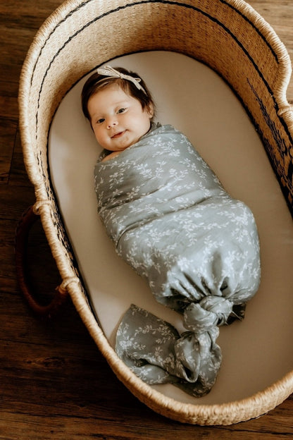 cute and chunky baby wearing a thin bow headband and wrapped with the bloom blue receiving blankets lying in her baby bassinet lined with a white cotton blanket