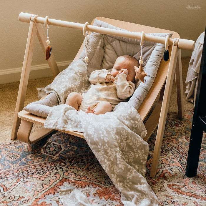 newborn baby placed in a wooden rocker covered with leafy sprig baby blanket