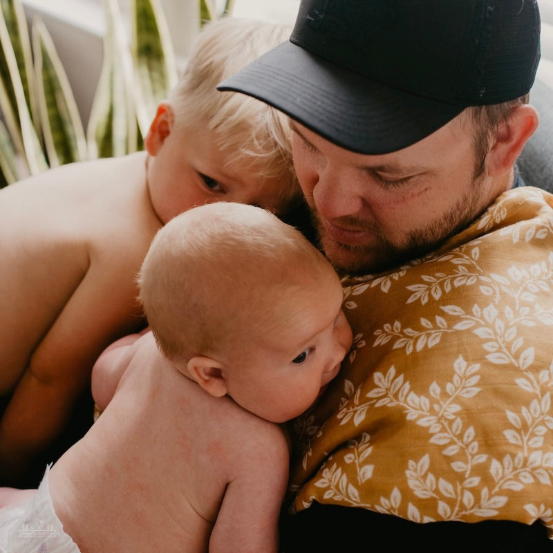 dad and his two adorable baby babies hugging each other while dad's right shoulder has the mustard leaf swaddle blanket used as a burp cloth