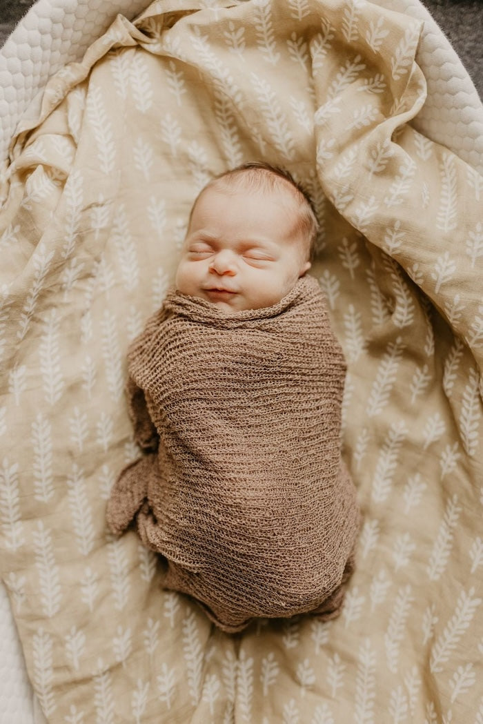 sweet little baby as cute as a button sleeping soundly and wrapped in a brown soft wool-like fabric laid on top of our cream baby blanket