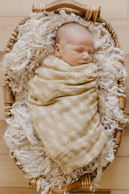 an image of a sleeping baby wrapped in our cream baby blanket nestled in a baby bassinet layered with an off-white fluffy rug