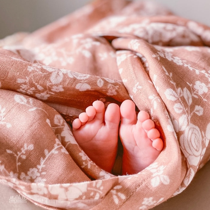 A baby wrapped in the Mini Wander Vintage Bouquet Sienna swaddle, revealing her adorable feet.
