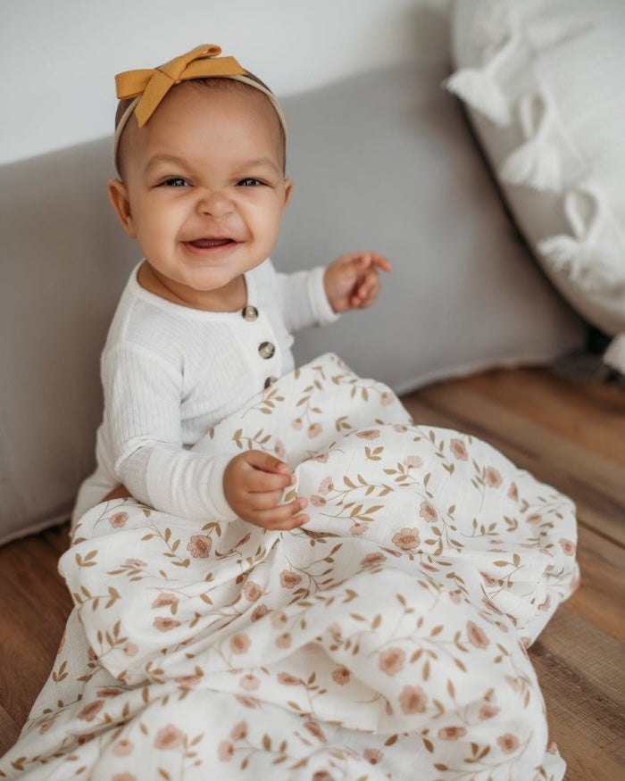 an adorable a happy baby wearing cute baby clothes smiling looking at the camera sitting with the floral baby blanket in her lap