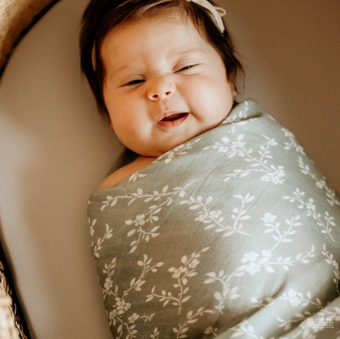 baby wrapped in the bloom blue floral muslin swaddle in a very happy mood