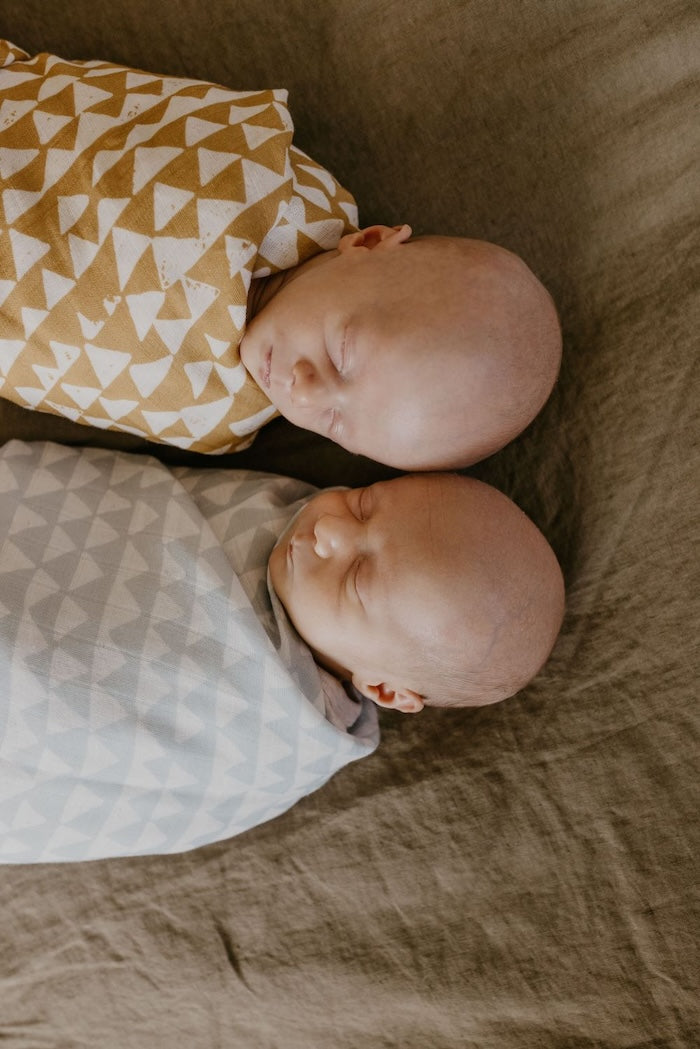 twin babies sleeping soundly wrapped in their yellow and blue triangle checks print swaddle
