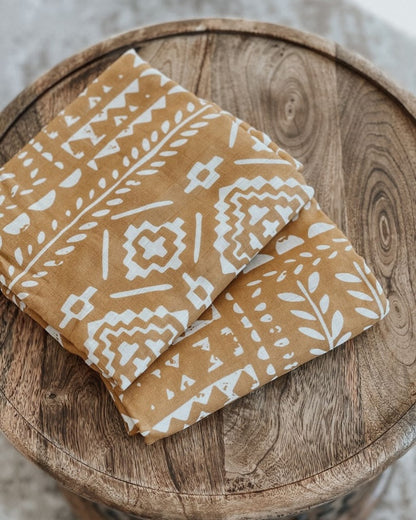 a photo of our boho dark yellow blanket folded on top of a wooden circular table, great newborn baby present