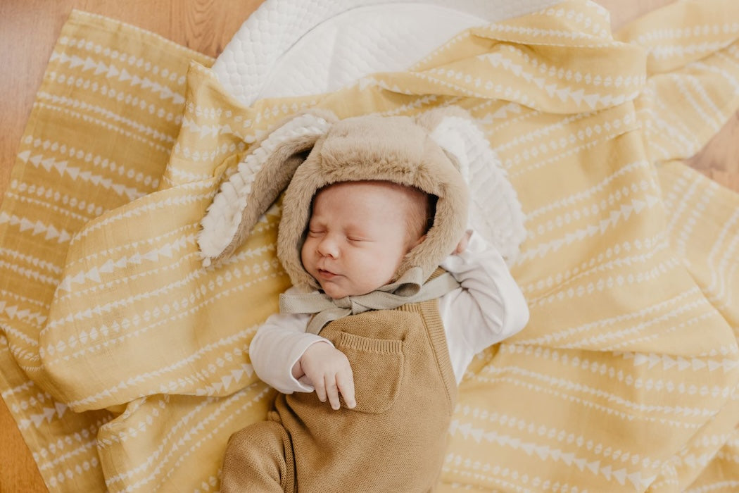 one of the best photos of our cute babies wearing his neutral colored baby jumper and his rabbit hat while relaxing over our dusty yellow aztec pattern swaddle used as a baby boy bedding