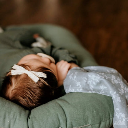 top view of a little baby wearing a white lace ribbon sleeping soundly and hugging her bloom blue floral muslin swaddle