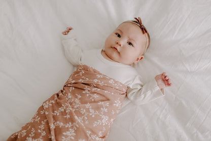 A photo of the baby in long sleeves and a swaddle decorated with bloom flowers from the waist down.