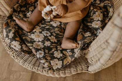 an image of a baby's hands and feet with the baby's feet resting in the flower swaddle that perfectly matches any newborn outfits and her hands holding a white and beige baby teether