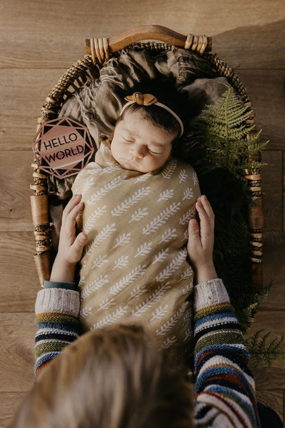 a beautiful image of a baby sleeping soundly in her baby bassinet wrapped in our cream baby blanket and her mom preparing and getting baby ready for her baby milestone photo
