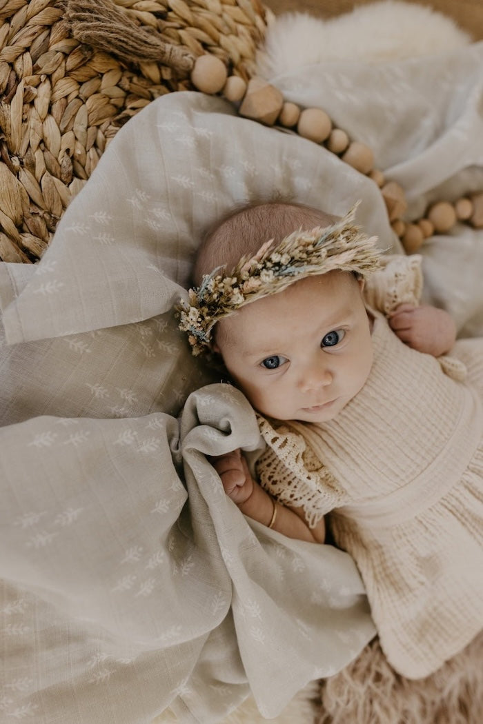 baby girl sitting on top of the newborn swaddle set wearing neutral colored dress and floral headband