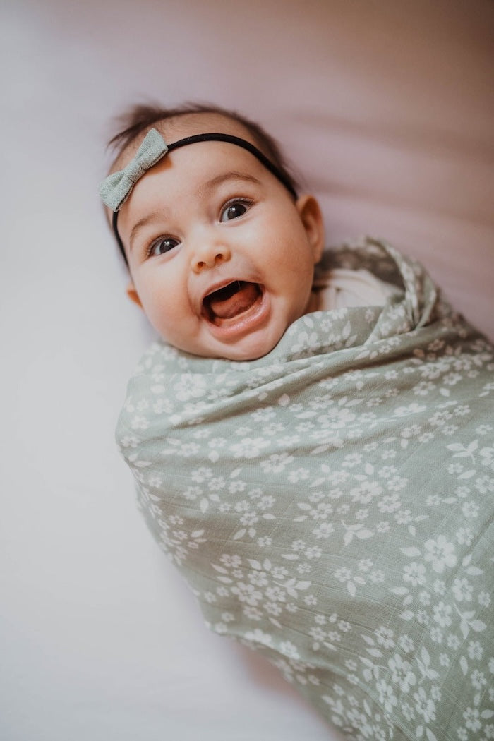 A blissful baby wrapped snugly in a floral sage green swaddle.