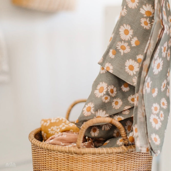 Daisy sage green swaddle hung alongside a buri basket and another floral swaddle.