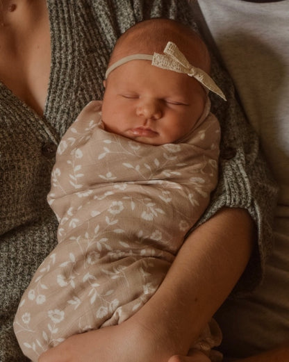 a precious moment of a lovely little baby wearing a white lace ribbon wrapped with the wildflowers taupe floral baby blanket held by her mom