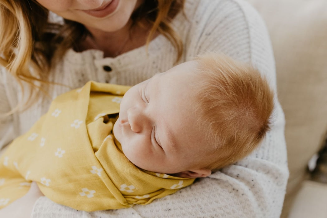 baby asleep in her mom's arms in a yellow baby blanket