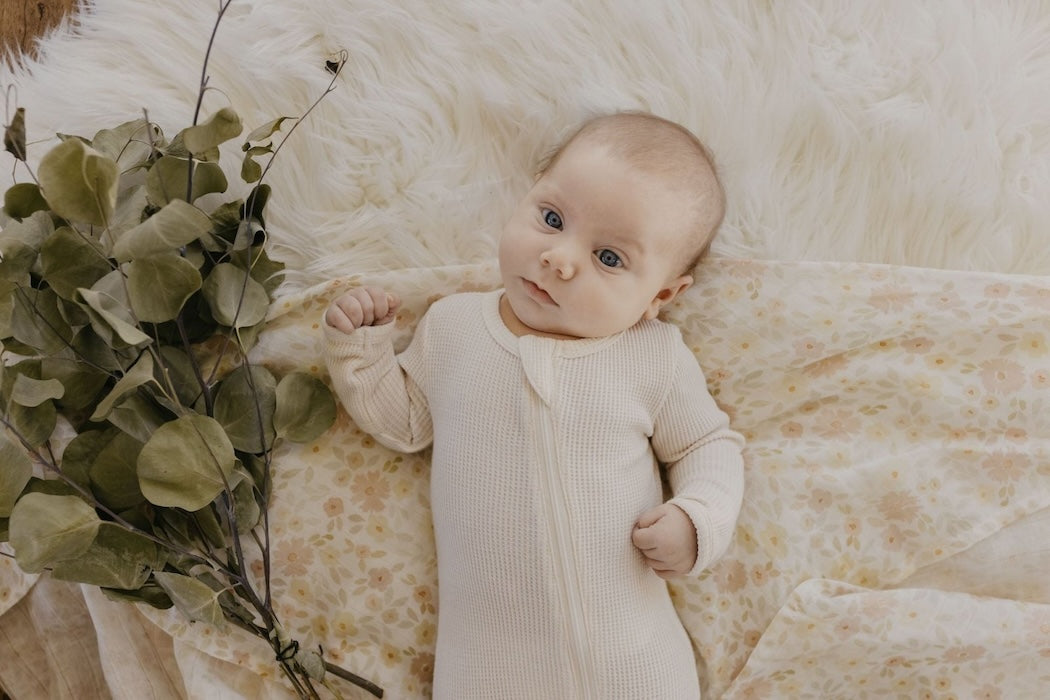 baby girl wearing white baby clothes lying in her meadow cream muslin swaddle as a photo background