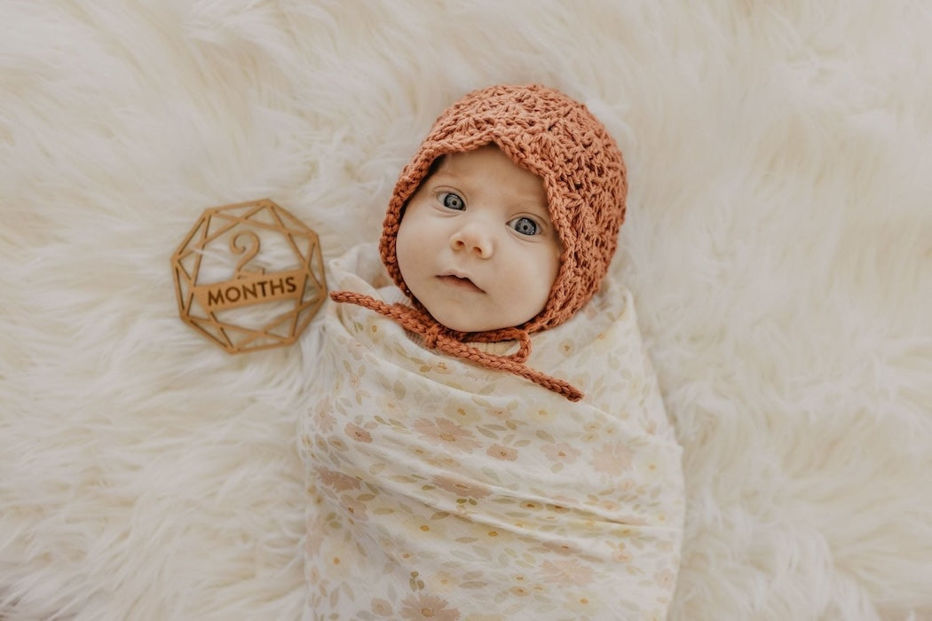 two month old baby girl in a bonnet in her baby milestone photo wrapped in natural cotton meadow cream