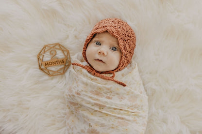 two month old baby girl in a bonnet in her baby milestone photo wrapped in natural cotton meadow cream