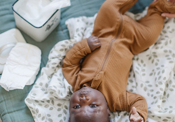 a baby boy is laying down, mama is getting ready to give him a diaper change. A multi purpose blanket is being used as a clean surface.