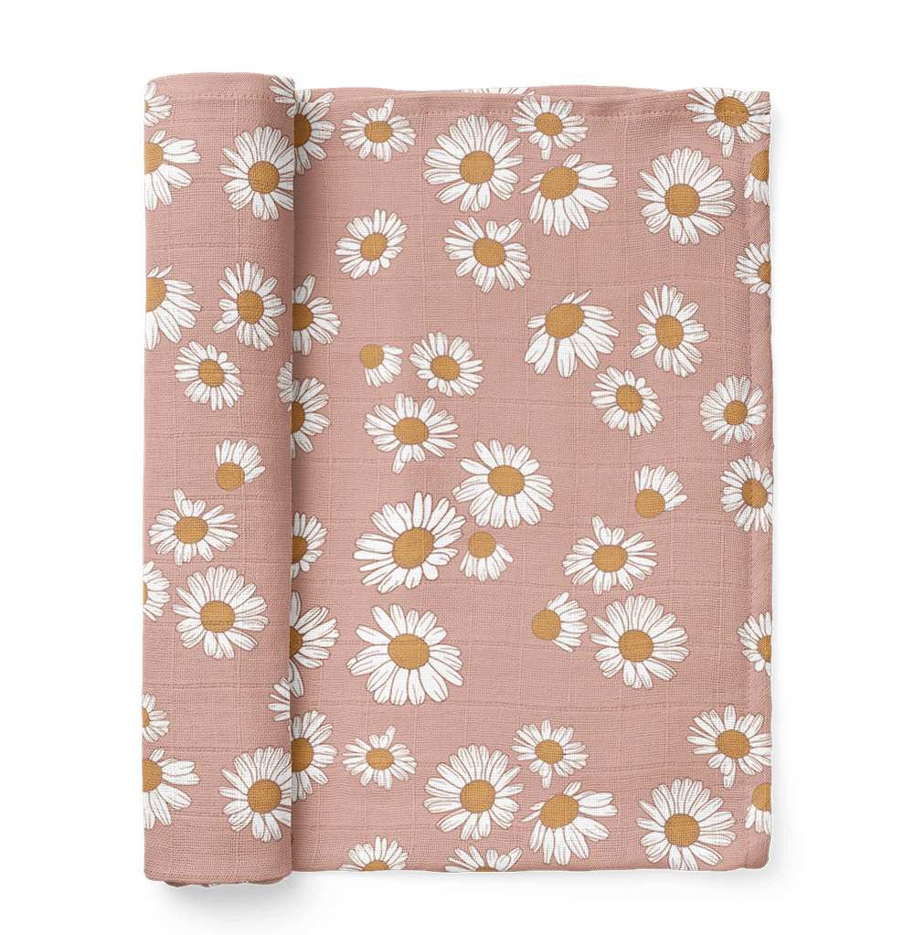 A half-rolled Mini Wander swaddle in soft blush pink with a daisy floral design.