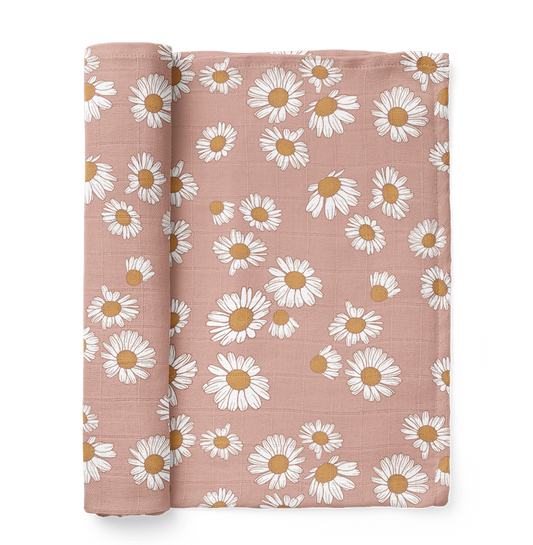 A half-rolled Mini Wander swaddle in soft blush pink with a daisy floral design.