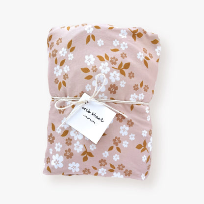 ersey polyester crib sheet with whimsy floral pattern in white and beige flowers, dark orange leaves on a dusty pink backdrop